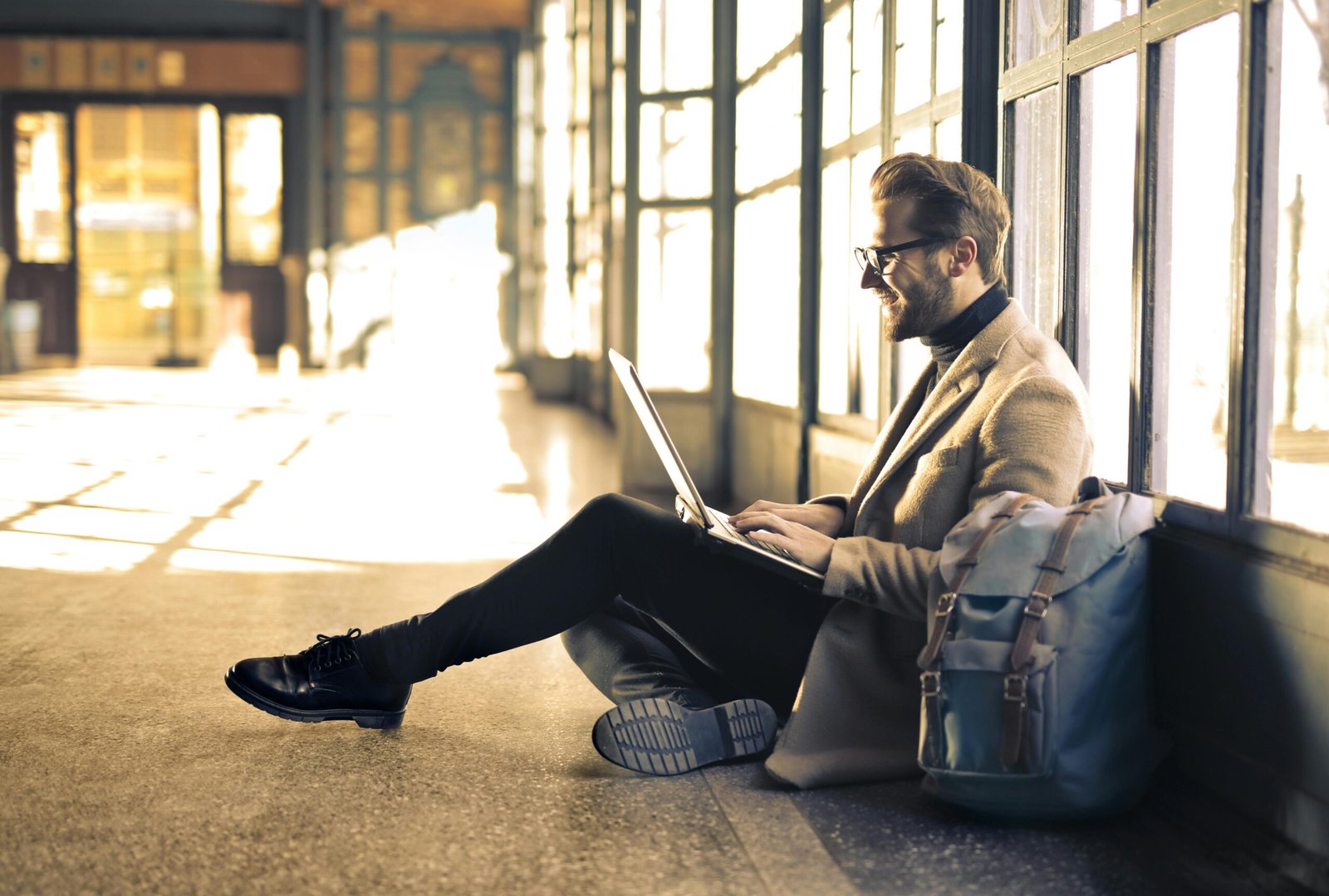 pexels-photo-838413-838413 Man sitting by a window at a Budapest train station, working on his laptop with sunlight streaming through.